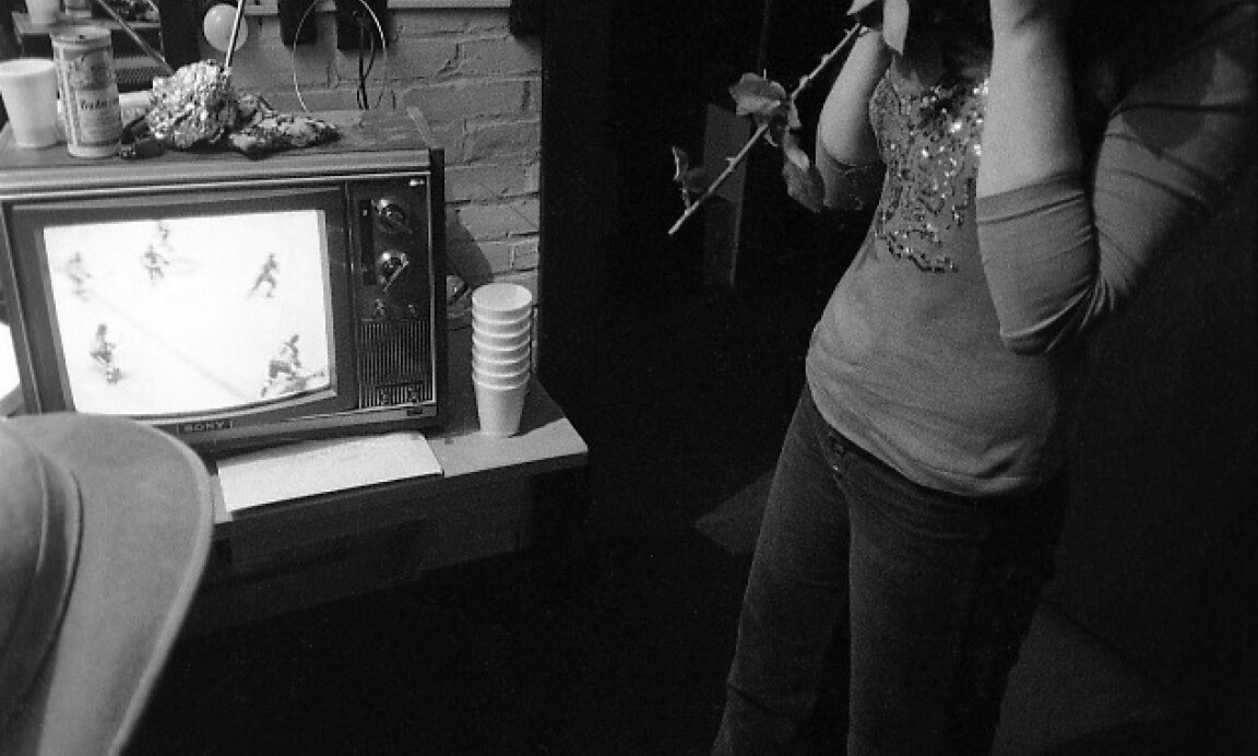 Bonnie Raitt backstage, clasping a rose and watching hockey on television at the Aquarius Theater, Boston, October 5, 1973