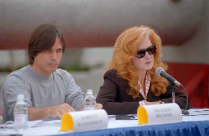 Jackson Browne and Bonnie Raitt at a press conference on the West Terrace of the Capitol in opposition to H.R. 1270, the Nuclear Waste Policy Act of 1997, which would allow for the transfer of radioactive waste to Yucca Mountain, Nevada. Behind them is a mock nuclear waste cask. 24 Sept. 1997